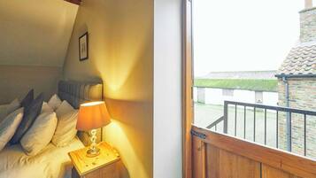 A bedroom with a bed, pillows, a bedside lamp, and a view of a brick building through a window.