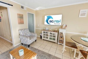 Ein Wohnzimmer mit einer Couch, einem Glastisch, einer Kommode mit Körben und einem Fernseher, der 'BIG FISH Rentals' anzeigt.