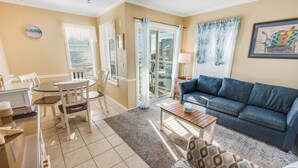 A living room with a blue sofa, a wooden coffee table, a patterned armchair, a dining table with chairs, and a view through a glass door to the outside. - North Myrtle Newly Remodeled Oceanfront View Suite (North Myrtle Beach)