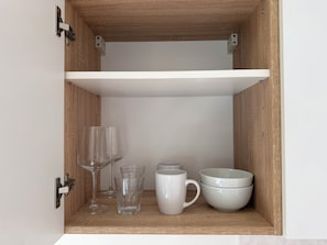 Un meuble en bois avec une étagère blanche contenant des verres transparents, une tasse blanche et des bols blancs.
