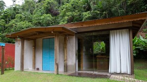Un pequeño edificio de una sola planta con puerta de vidrio y puerta azul, rodeado de abundante follaje.