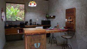 Una cocina rústica con mostrador de madera, lámpara colgante, ventana con vista a follaje y un armario de madera con detalles decorativos.