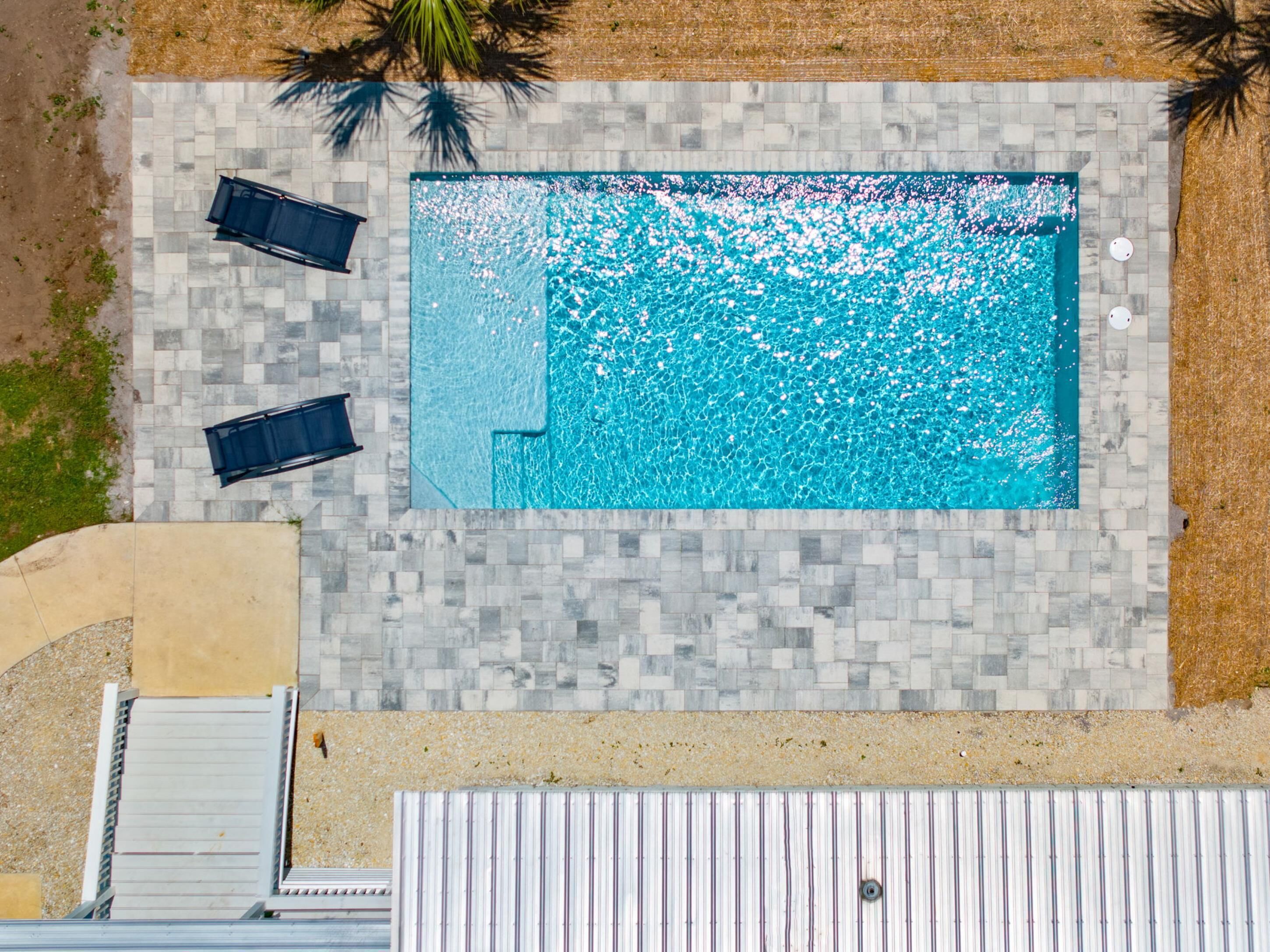 An aerial view of a rectangular swimming pool with a tiled deck surrounding it.