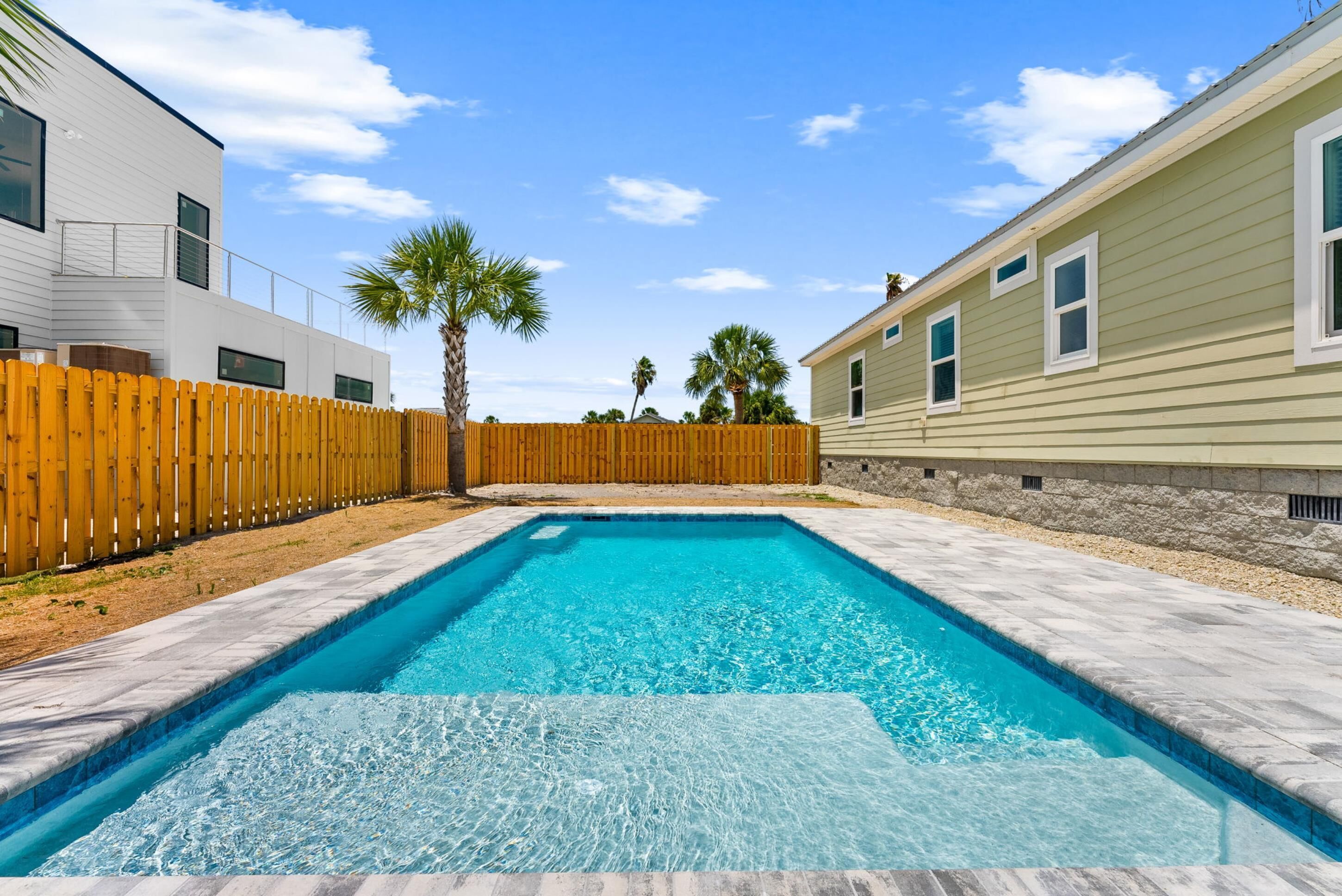 A rectangular swimming pool with clear blue water, surrounded by a wooden fence and a stone wall.
