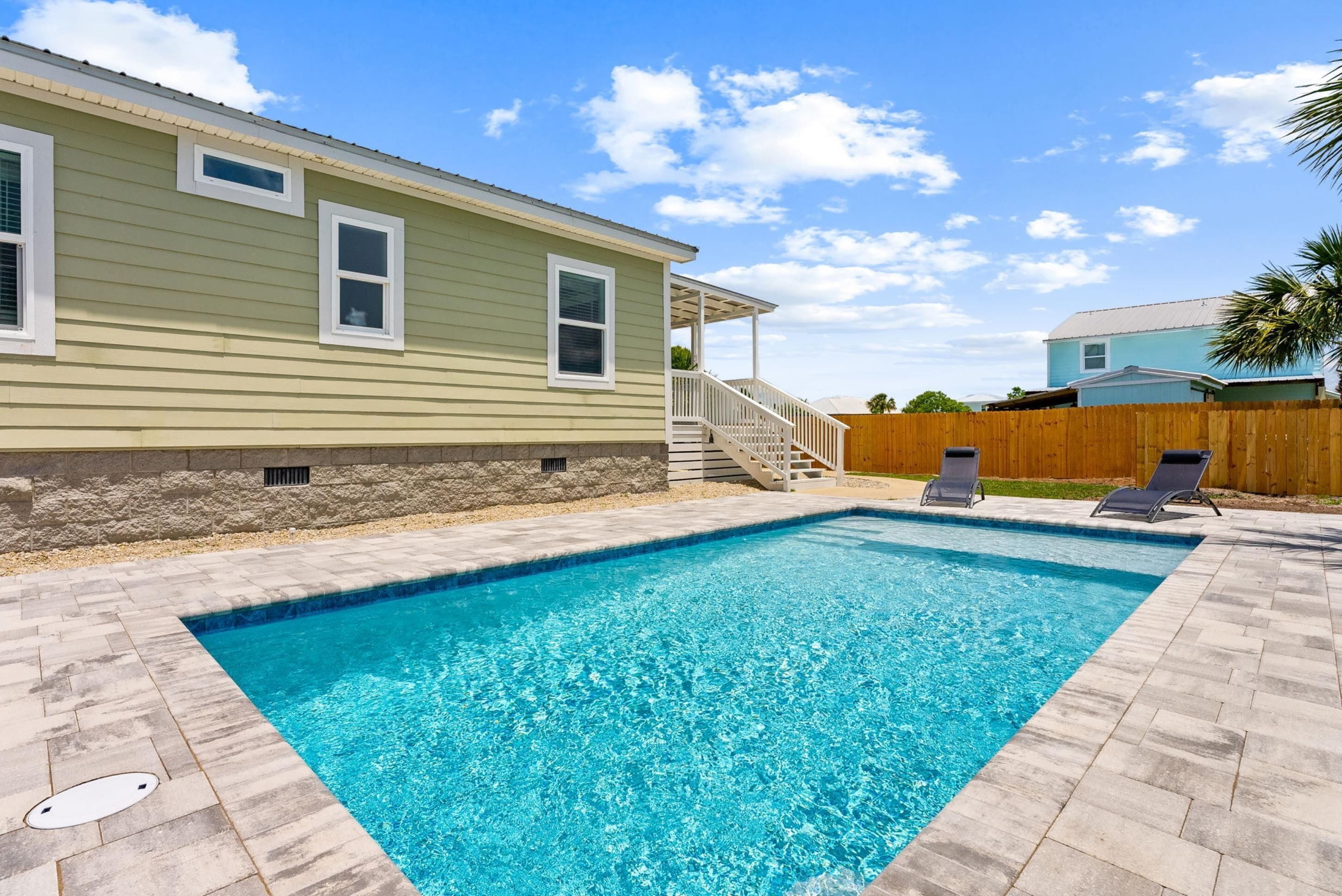Une piscine bordée de pierres, une terrasse en bois et une maison avec un porche.