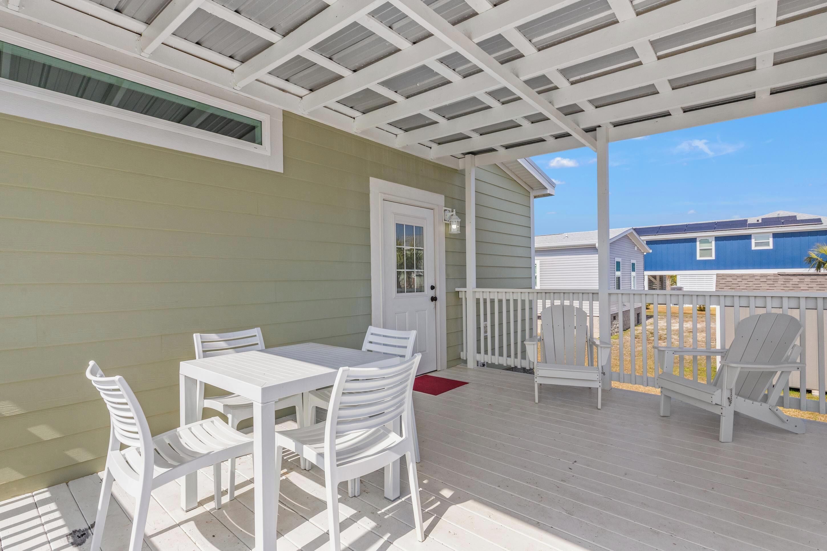 A covered patio with a white table and chairs, a white door, and a view of neighboring houses.