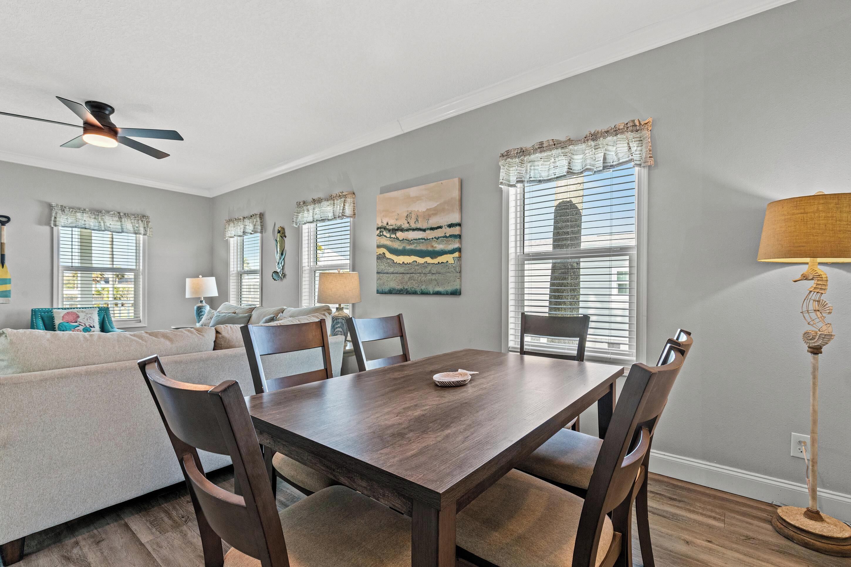 A dining area with a wooden table and chairs, a ceiling fan, and artwork on the walls.