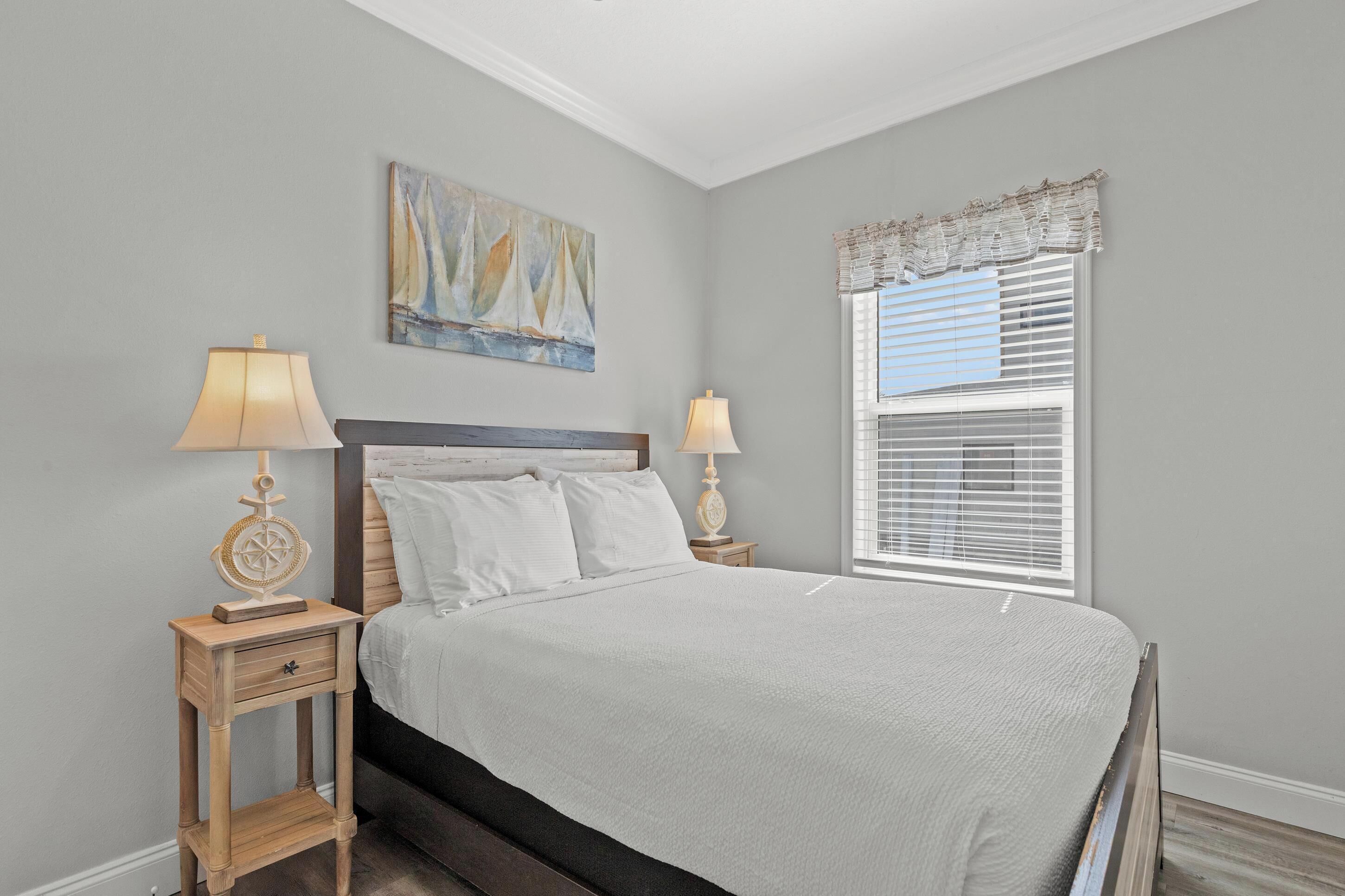 Une chambre à coucher comprenant un lit, deux tables de chevet, une commode, une fenêtre avec des stores et un tableau accroché au mur.