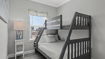 A bunk bed in a room with a window, a small bedside table with a lamp, and a framed picture on the wall.
