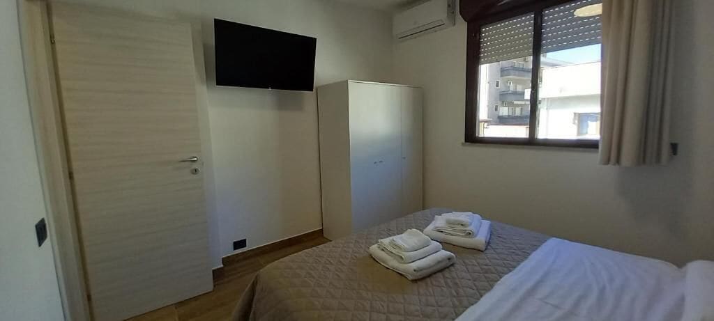 A hotel room with a bed, a wardrobe, a television mounted on the wall, and a window with curtains.