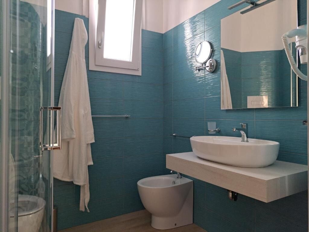 Un baño con cabina de ducha de vidrio, inodoro blanco, bidé y lavamanos con espejo superior.