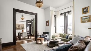 A spacious living room with a leather sofa, a coffee table, and a dining area visible through an open doorway. - Cozy Downtown Victorian- Prime Location- Hot Tub- Billiards (Indianapolis)
