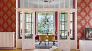 Une porte ouverte donne sur un espace repas comprenant une table, des chaises et un lustre.