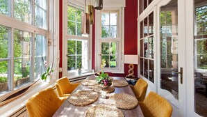 Une salle à manger avec une grande table, des chaises jaunes et une vue sur l’extérieur grâce à de grandes fenêtres.