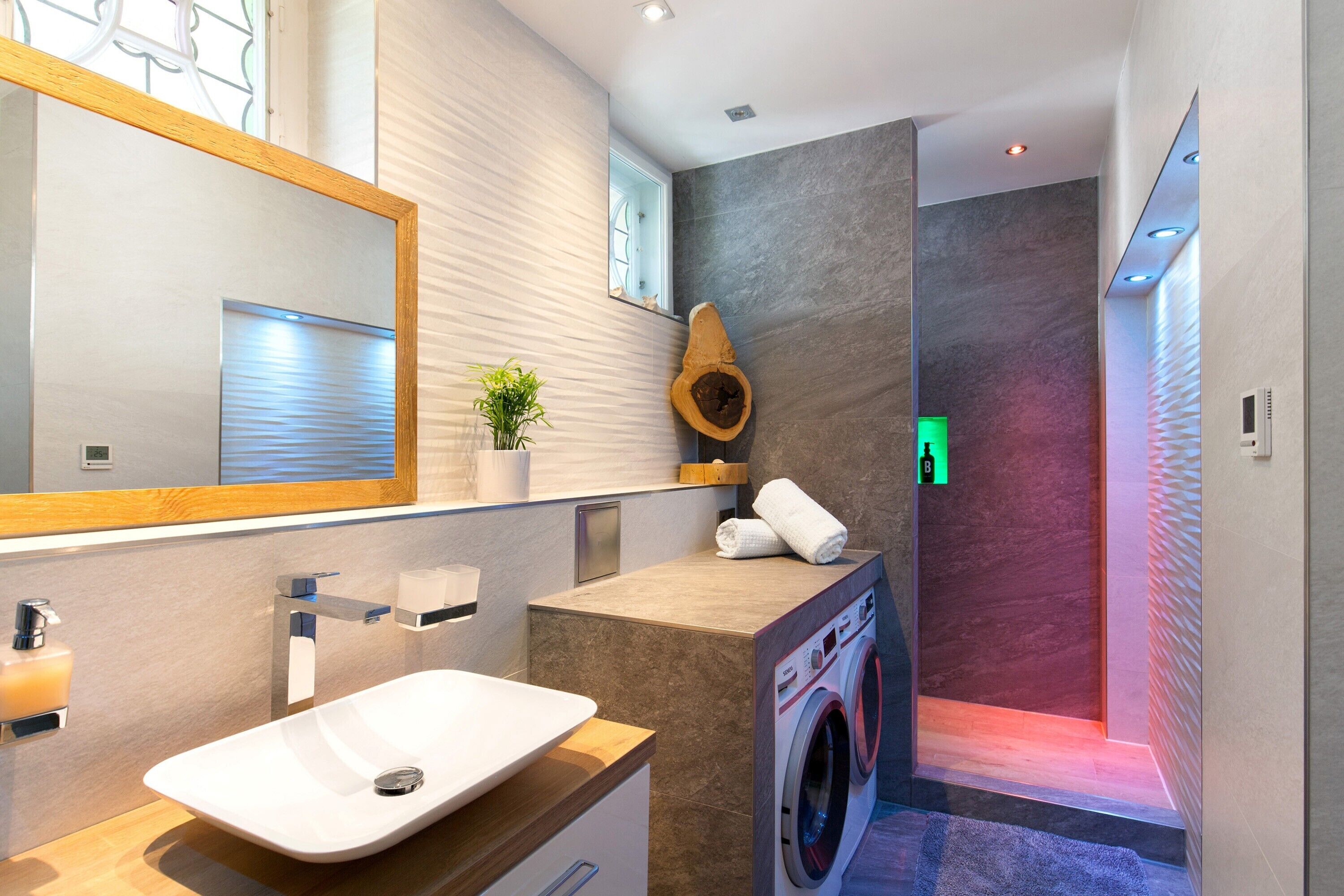 Uma casa de banho moderna com um espelho grande, uma pia, um porta-toalhas, uma planta e uma máquina de lavar roupa.
