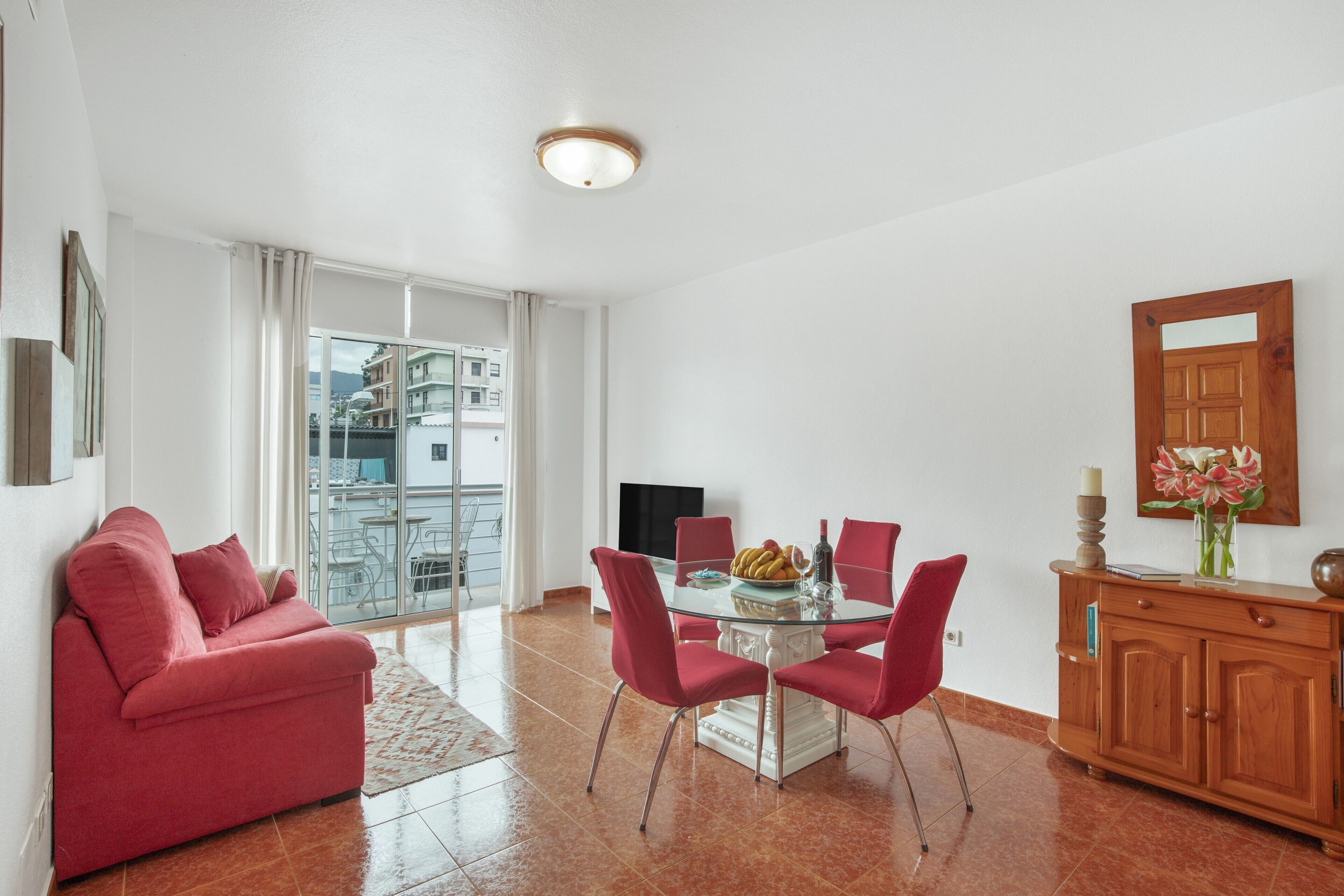 Uma sala de estar moderna com uma mesa de jantar de vidro, cadeiras vermelhas, um sofá vermelho e um armário de madeira.