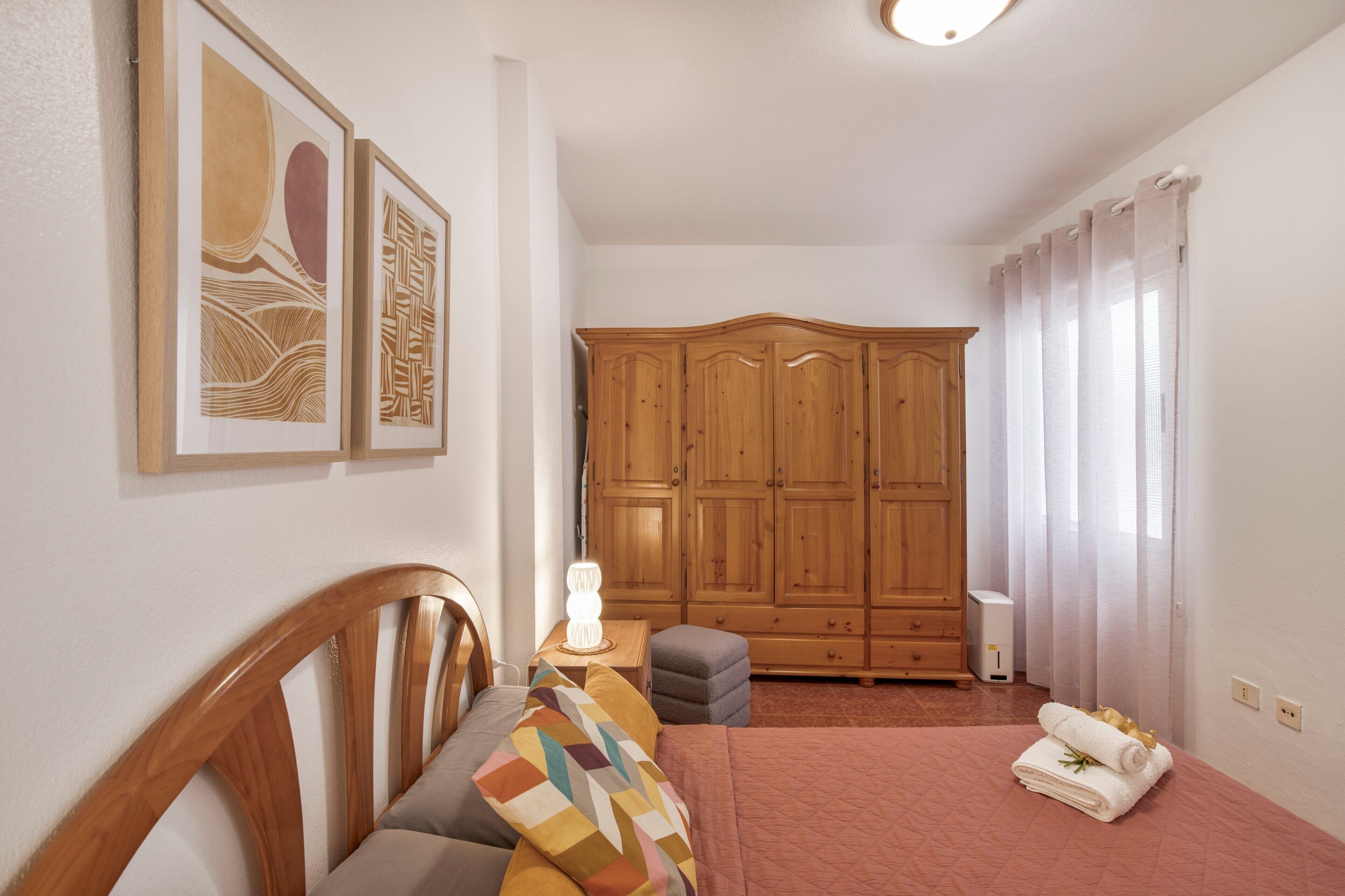 Een slaapkamer met een houten garderobe, een bed met een bedekt deksel, en twee kunstwerken in lijsten aan de muur.
