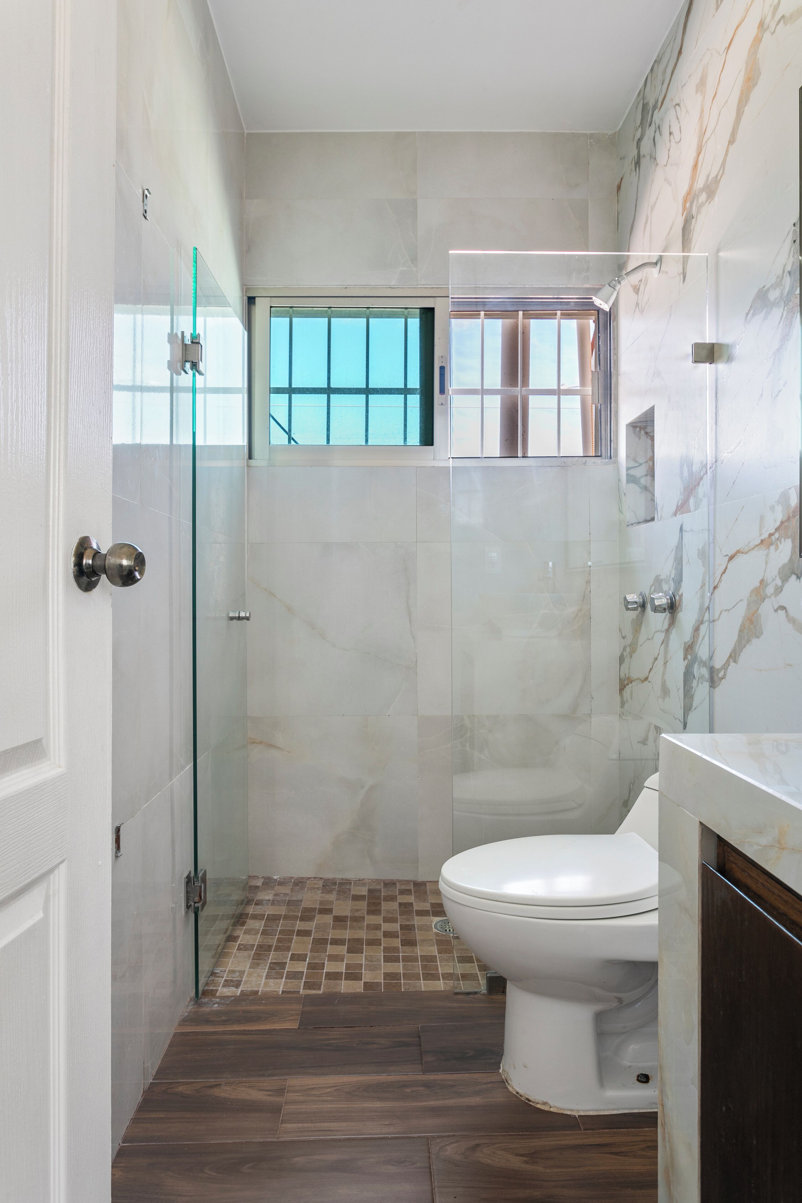 Une salle de bain avec une douche à parois de verre, des toilettes et un mur en marbre.