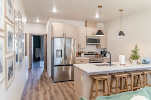 Una cocina moderna con electrodomésticos de acero inoxidable, taburetes de madera y luminarias colgantes.