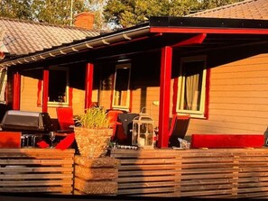Ein Holzhaus mit überdachter Veranda, roten Akzenten und einem Grill.