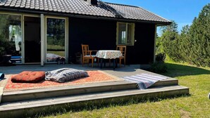 Ein Haus mit Ziegeldach, einer überdachten Terrasse mit Tisch und Stühlen und einem kleinen Garten.