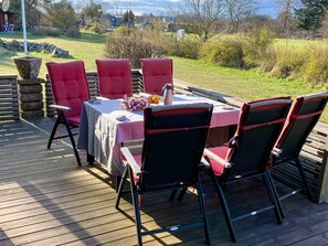 Zona pranzo all'aperto con tavolo e sedie, un fioriere in pietra e vista sul paesaggio circostante.
