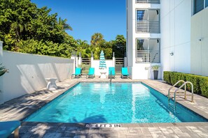 Une piscine dont la profondeur est indiquée à 4 pieds et 3 pouces, entourée d’un mur blanc, avec un parasol bleu et des chaises en arrière-plan.