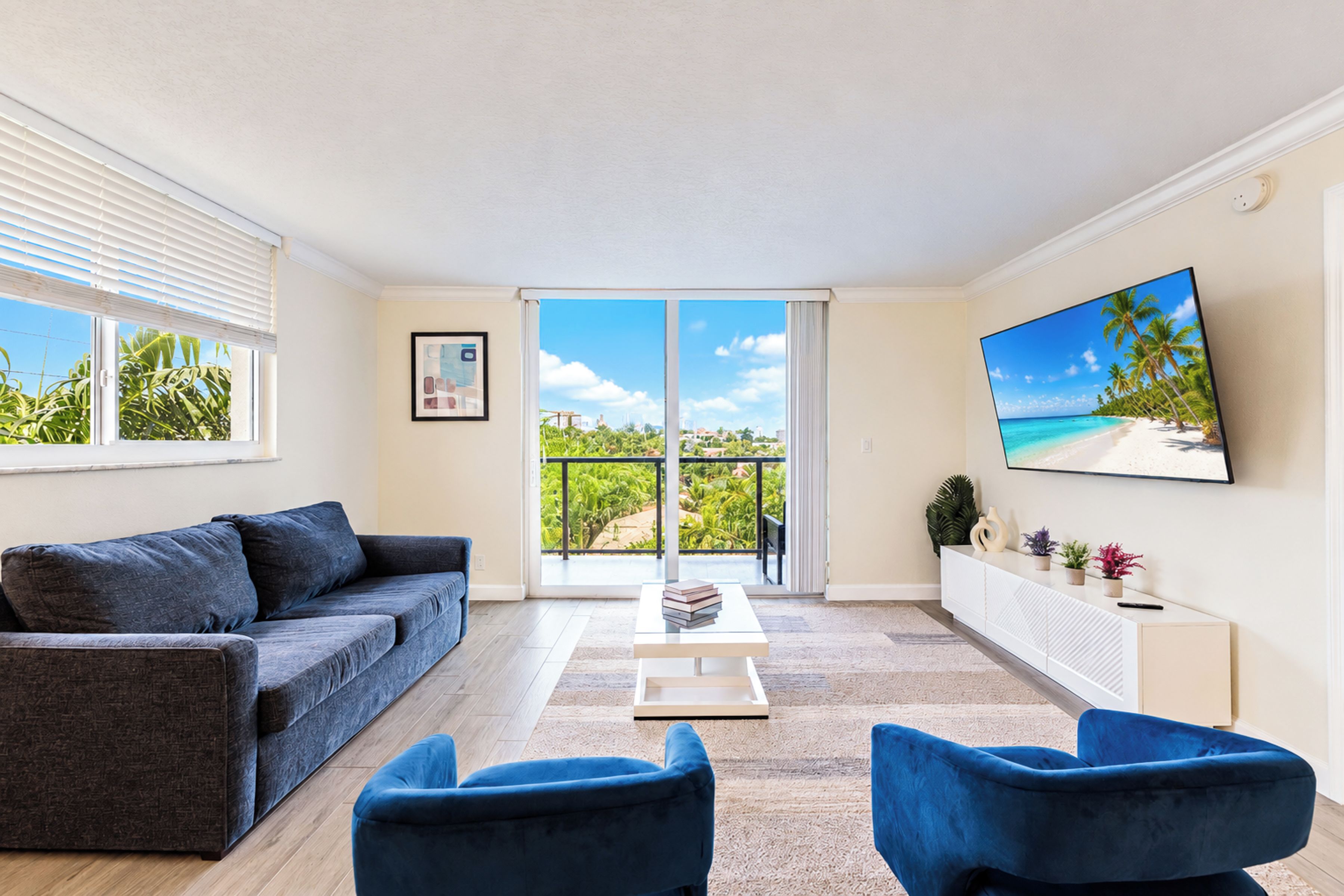 Un salon moderne avec un canapé, deux fauteuils, une table basse et un téléviseur fixé au mur.