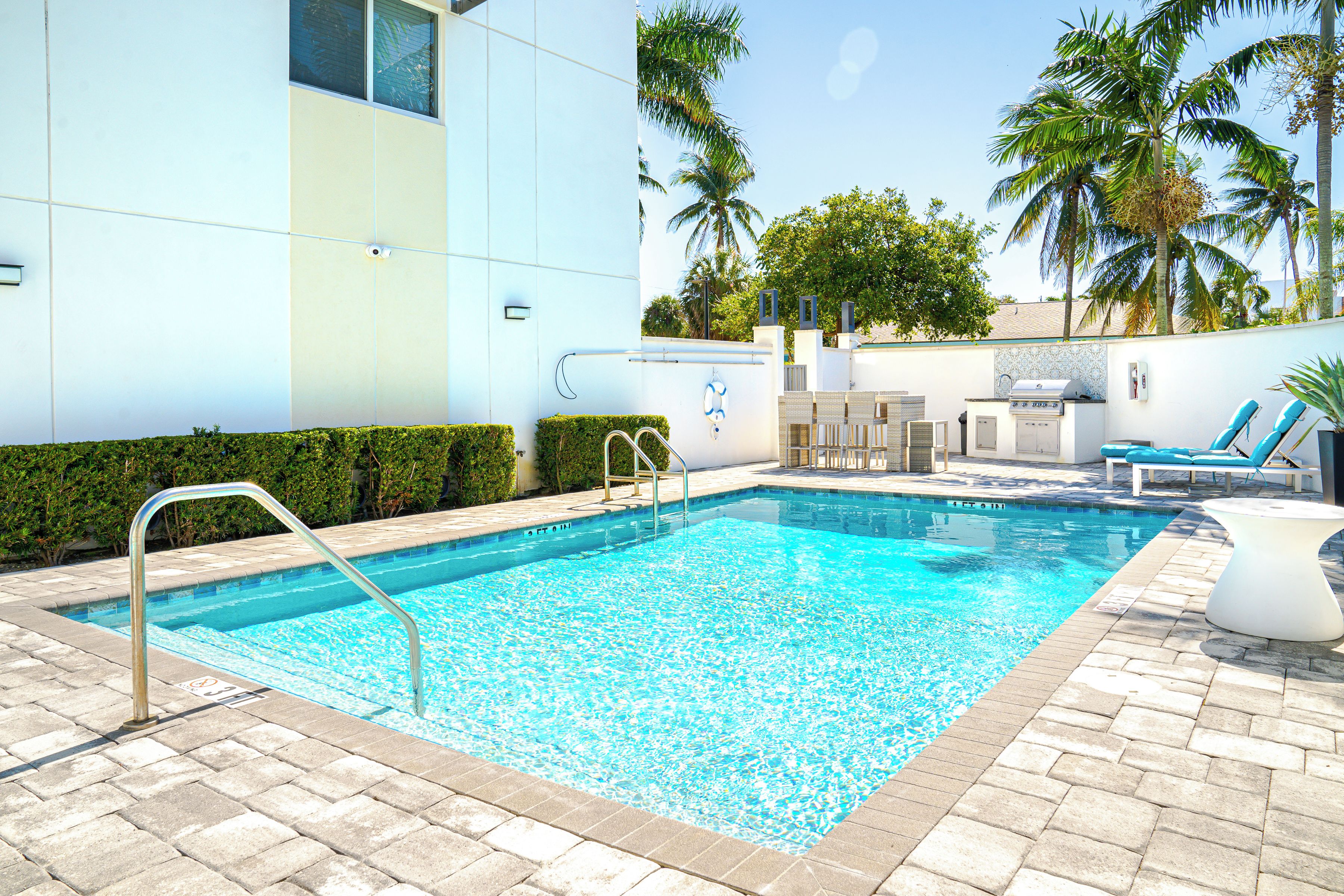 A swimming pool with a metal ladder, a barbecue area, and lounge chairs.