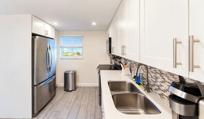 A modern kitchen with stainless steel appliances, a window with blinds, and a tiled backsplash. - Coastal Retreat: Directly Across from Beach w/ Heated Pool & 2 King Suites (Boca Raton)