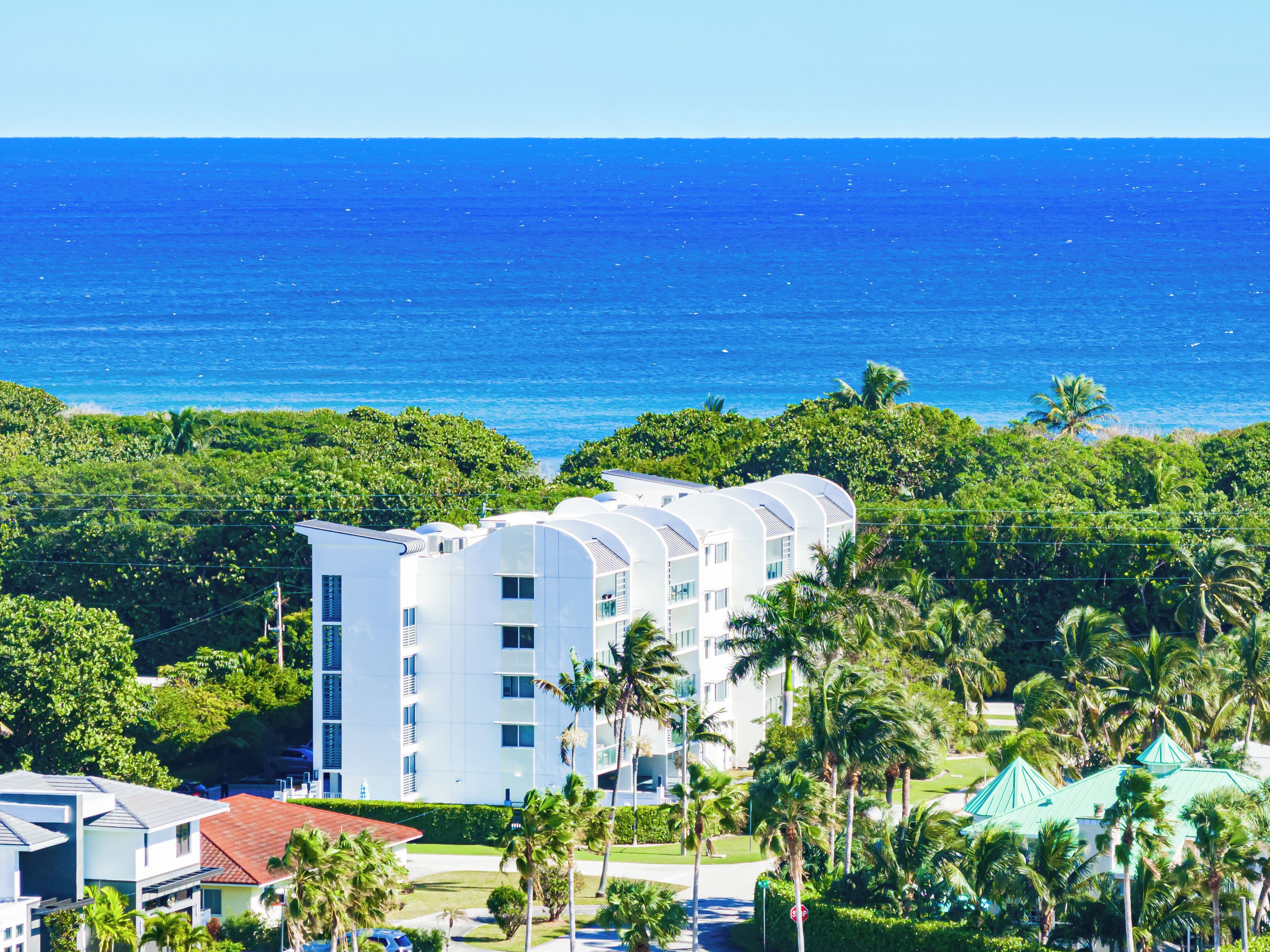 A modern hotel with multiple floors, surrounded by lush greenery and a view of the ocean.