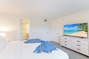 A hotel room with a bed, a TV displaying a beach scene, and a door leading to a bathroom. - Coastal Retreat: Directly Across from Beach w/ Heated Pool & 2 King Suites (Boca Raton)