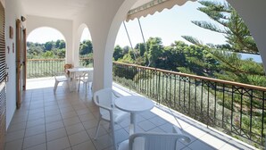 Un balcon avec des chaises blanches et une table, offrant une vue panoramique sur des arbres et une étendue d’eau.