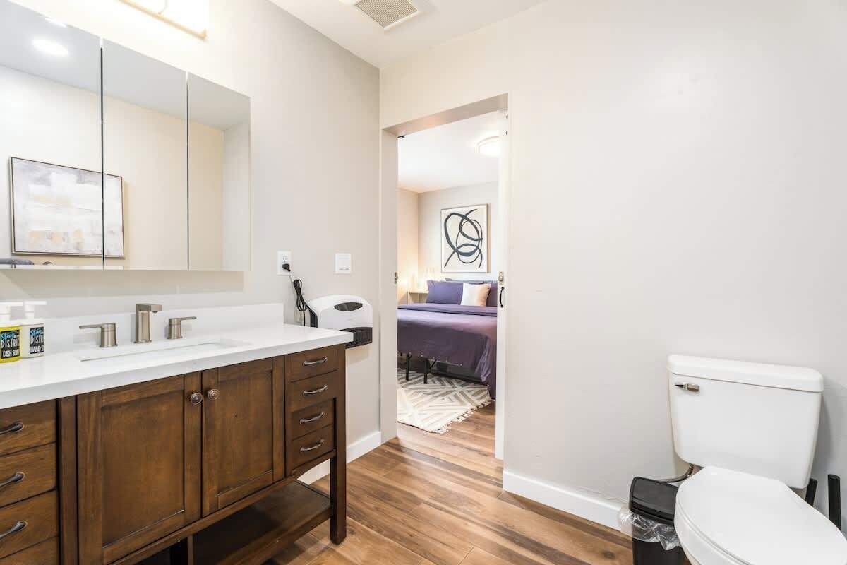 Ein modernes Badezimmer mit einem Holzwaschtisch, einer weißen Toilette und einem Bett im Hintergrund.