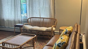 A living room with a brown leather sofa, a wicker chair, a small table, and a floor lamp. - Cornwall Cottage | Spacious, Fully Furnished Home for Corporate & Extended Stays (St. John's)