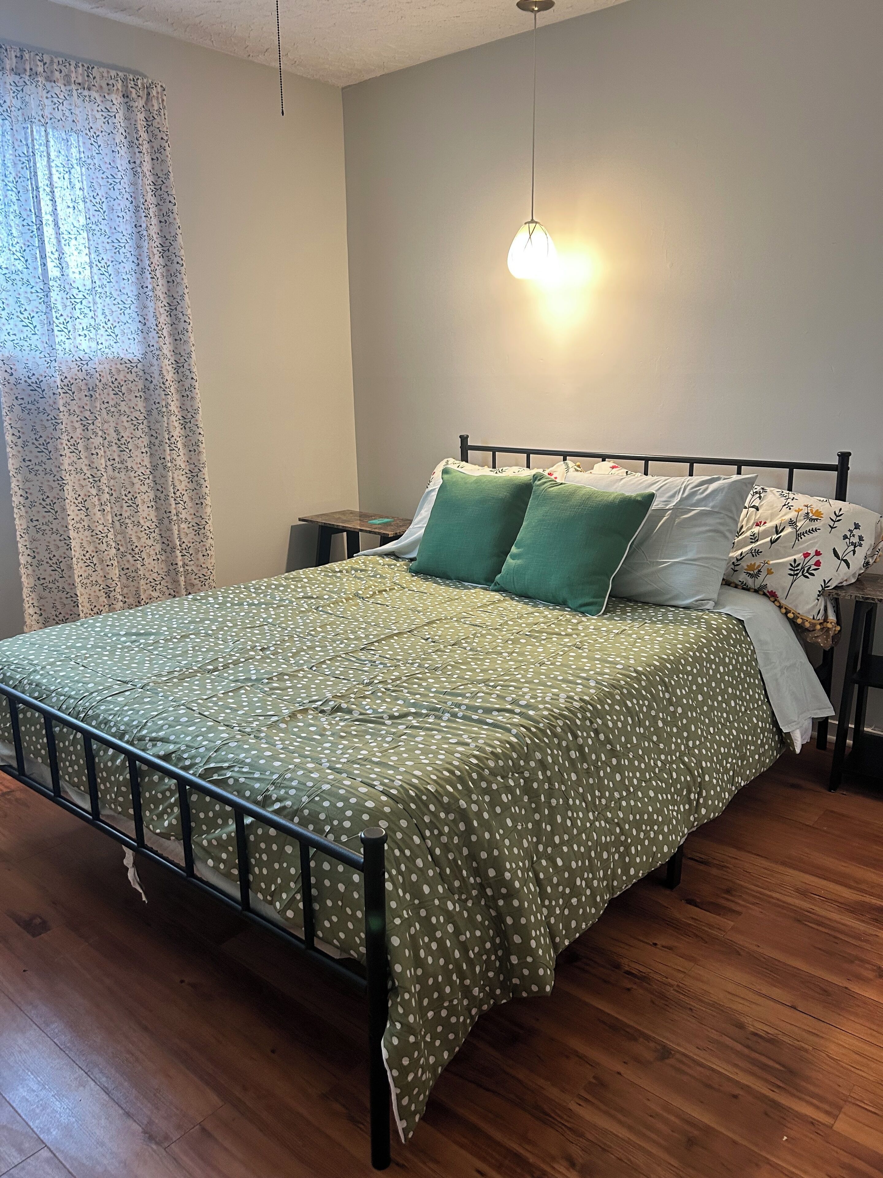 A bedroom with a bed, a nightstand, a lamp, and a window with curtains.