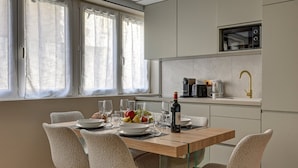 Eine moderne Küche mit Essbereich. Sie beinhaltet einen Holztisch mit Stühlen, eine Obstschale, Weingläser und eine Weinflasche.