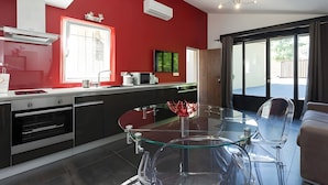 Een moderne keuken met een glazen eettafel, roestvrijstalen apparatuur en een rode accentmuur.