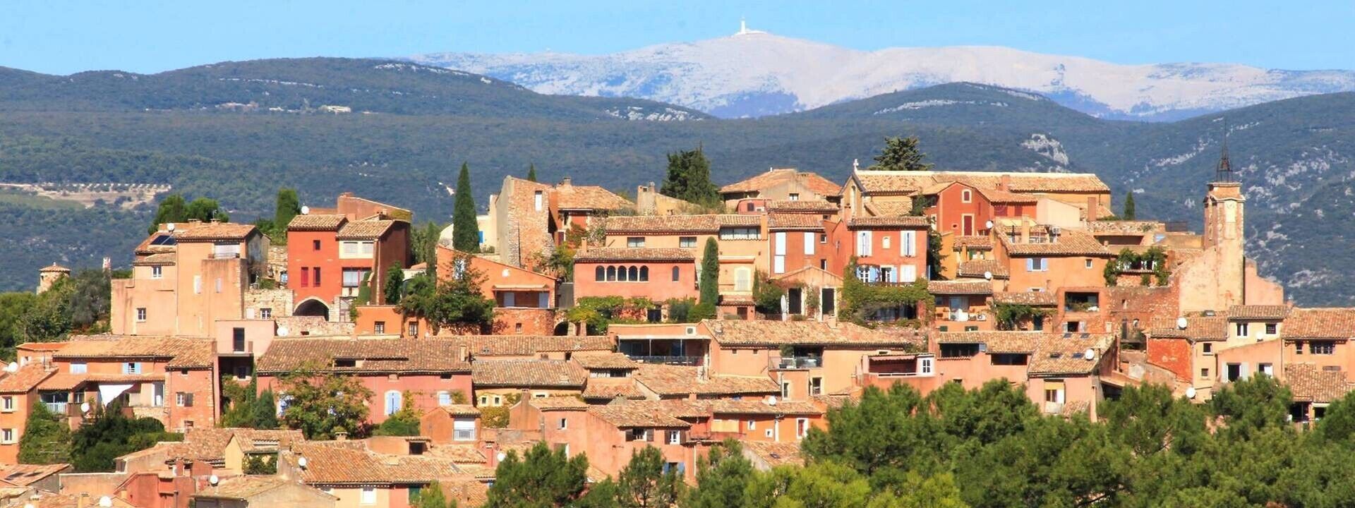 Un village perché sur une colline, doté d’une architecture traditionnelle, d’un clocher d’église imposant et surplombé par une chaîne de montagnes.