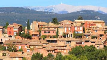 Un village perché sur une colline, doté d’une architecture traditionnelle, d’un clocher d’église imposant et surplombé par une chaîne de montagnes.