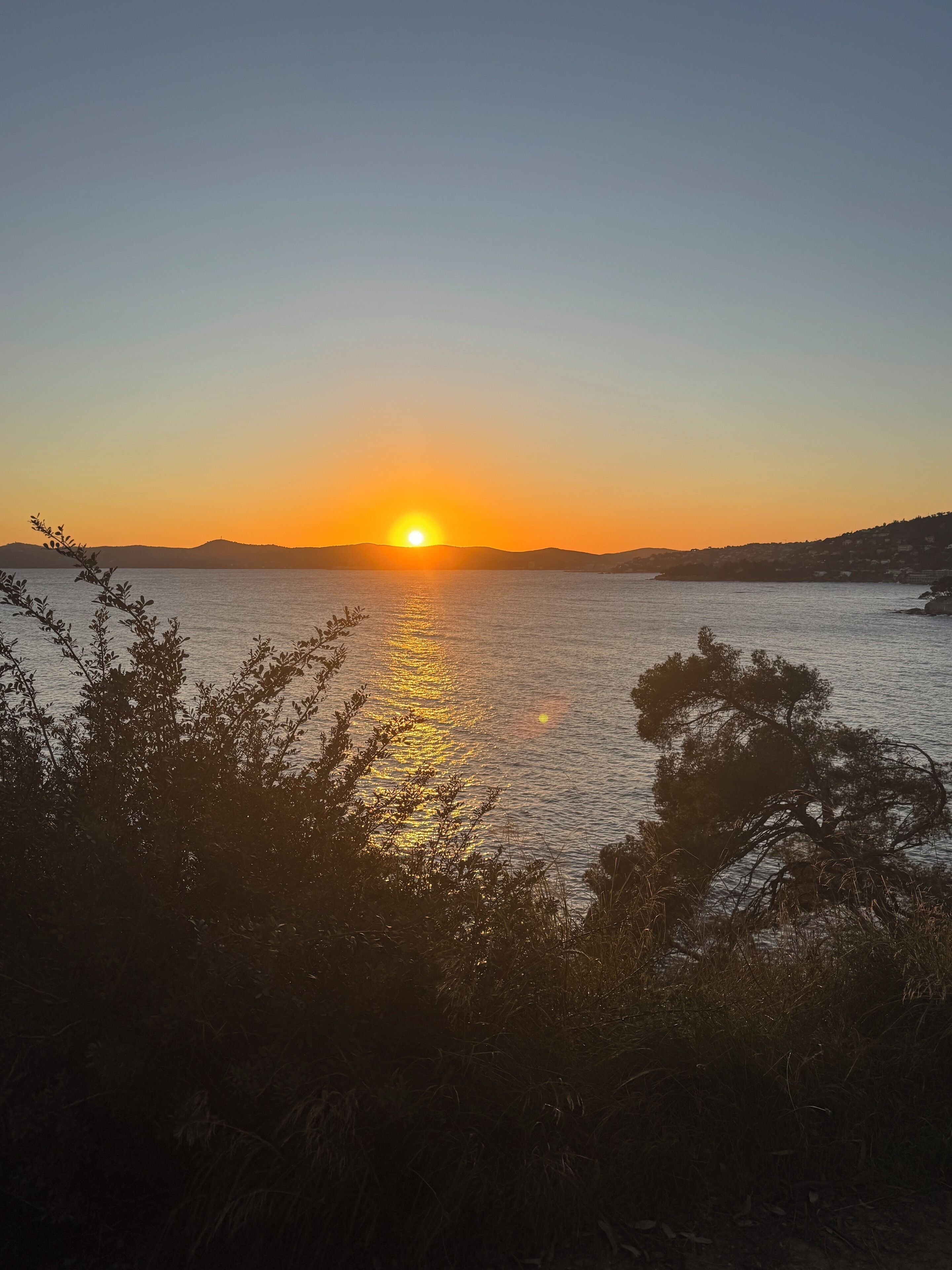 Un atardecer sobre una superficie de agua tranquila, con siluetas de colinas al fondo.