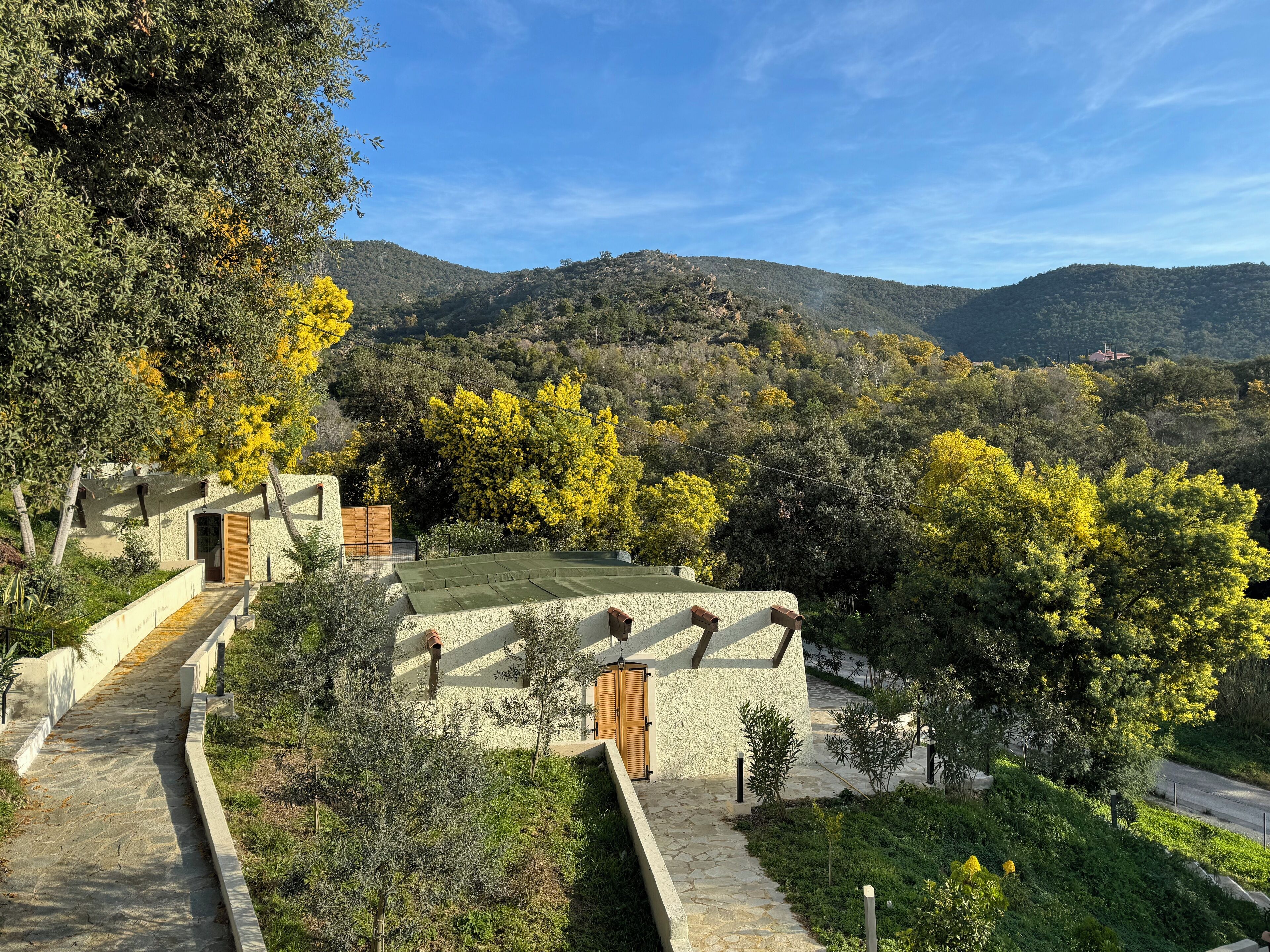 Un bâtiment en pierre surmonté d’un toit végétalisé, entouré d’arbres et de collines.