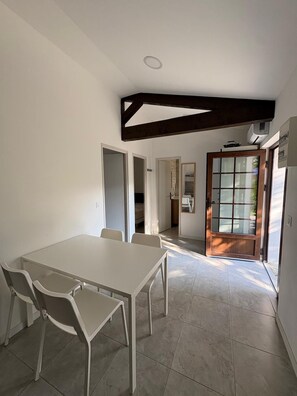 A dining area with a white table and chairs, a wooden ceiling beam, and a door leading to another room.