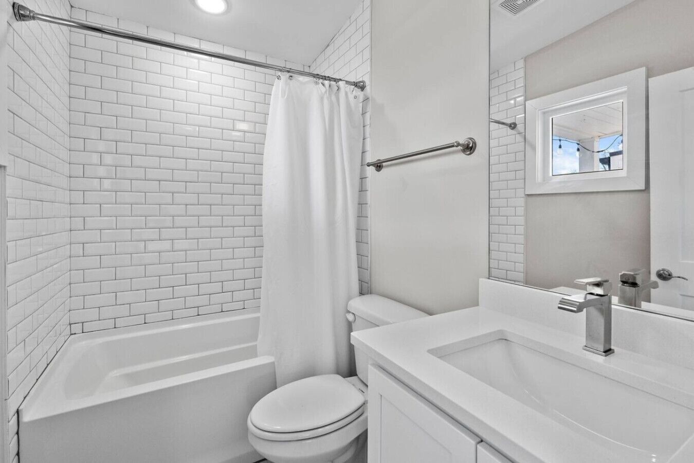 Une salle de bain moderne avec des carreaux de céramique blancs rectangulaires, une baignoire blanche, des toilettes et un lavabo avec un miroir.