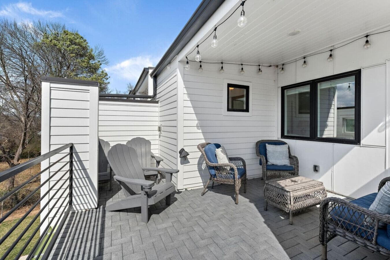 Un patio techado con sillas Adirondack y un sofá de mimbre, una ventana pequeña y una pared exterior blanca.