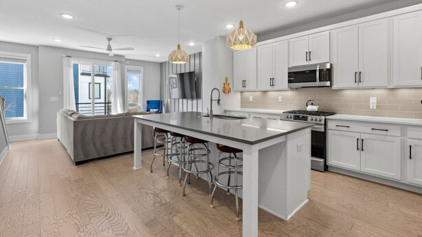 A modern kitchen with white cabinets, a central island with bar stools, a microwave, stove, and a large window. - Lucky #7 Hip East Nash Townhome + Rooftop Deck (Nashville)
