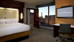 Une chambre d’hôtel avec un grand lit, un bureau, une chaise et un écran de télévision affichant le nom de l’hôtel.