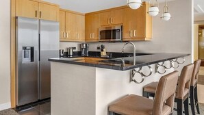 Une cuisine moderne avec des meubles en bois, des appareils électroménagers en acier inoxydable et un îlot central doté de tabourets de bar.