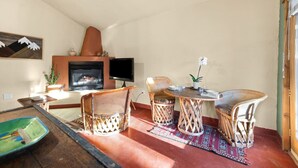 A cozy living room with a fireplace, wicker furniture, and a flat-screen TV. - Estrella De Oro Residences: Casita- Walk to town! (Golden)