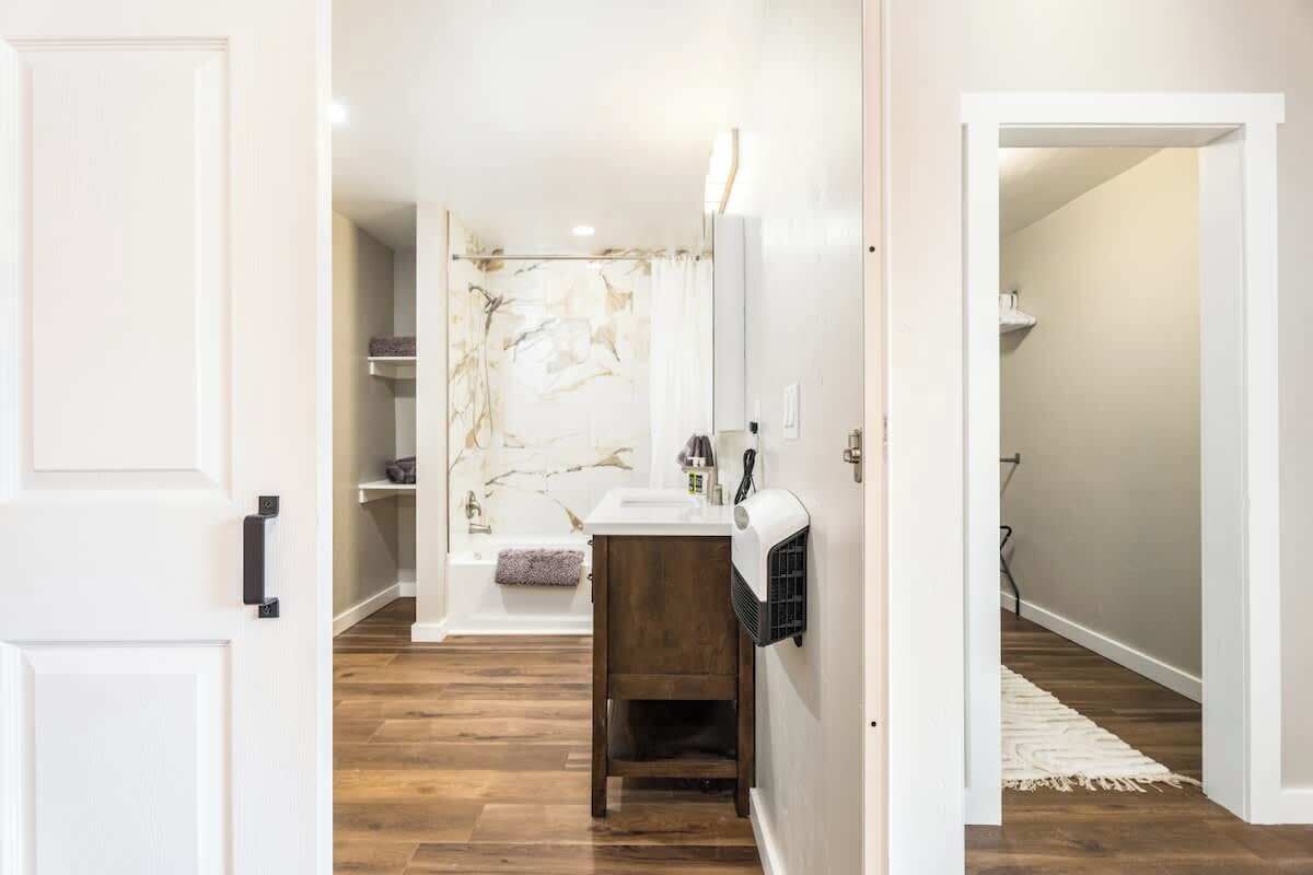 Un baño moderno con salpicadero de mármol, un lavabo blanco y un mueble de tocador de madera.